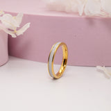 A gold ring with a solid inlay featuring breastmilk, displayed on a pink surface with floral accents.