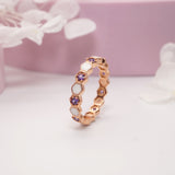 An elegant sterling silver ring with a honeycomb-inspired pattern, featuring preserved breastmilk inlays and purple birthstone cubic zirconia accents, displayed against a pink background with floral elements.